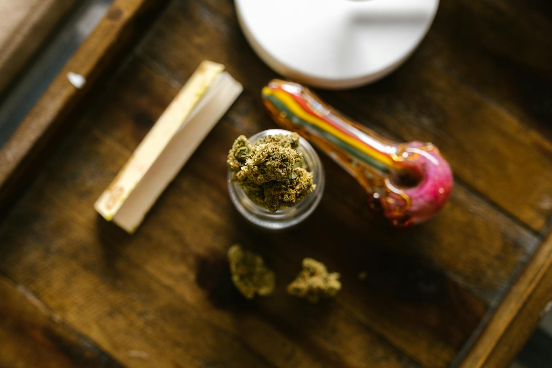 Close-up of cannabis flower, a smoking pipe and papers on a table. Source - Pexels